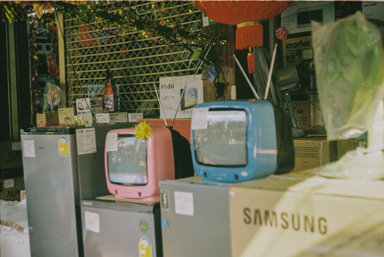 A storefront display featuring vintage televisions and home appliances on a sunny day in Bangkok.